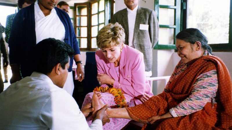 Princess Diana sitting and speaking with people affected by leprosy during a hospital visit, showing a moment of direct human connection.